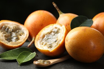 Ripe passion fruits, green leaves and seeds on black table, closeup