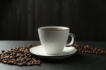Aromatic coffee in cup and beans on black table, closeup