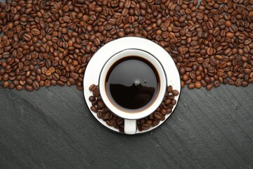 Aromatic coffee in cup and beans on black table, flat lay