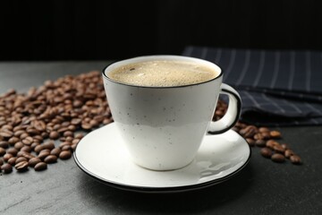 Aromatic coffee in cup and beans on black table, closeup