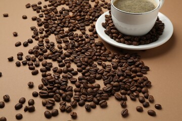 Aromatic coffee in cup and beans on beige background, closeup