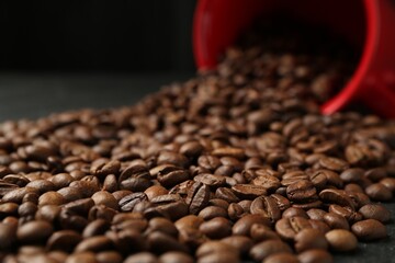 Aromatic coffee beans and overturned cup on table, closeup