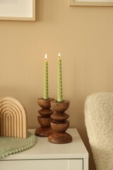 Stylish candlesticks with burning candles and other decor on cabinet near beige wall indoors