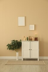 Stylish candlesticks with burning candles and other decor on cabinet near beige wall indoors