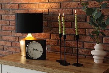 Candlesticks with burning candles on table near brick wall