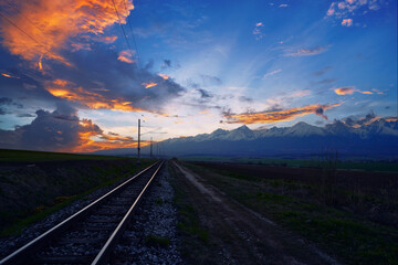 Railway Tracks Leading to Snowy Mountains at Sunset With Dramatic Clouds..