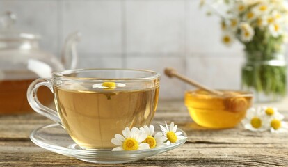 Delicious chamomile tea in glass cup, fresh flowers, honey and teapot on wooden table, closeup