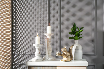 Elegant candlesticks with burning candles, branches in vase and other decor on dresser near grey...