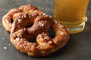 Tasty pretzels and glass of beer on dark textured table, closeup
