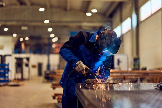 Worker Performing Welding in Industrial Workshop with Spark Effects