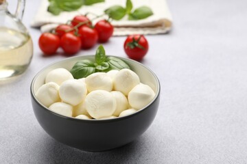 Tasty mozzarella cheese balls, tomatoes and basil on light grey table, closeup. Space for text