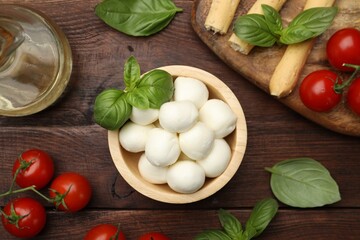 Tasty mozzarella cheese balls, tomatoes and basil on wooden table, flat lay