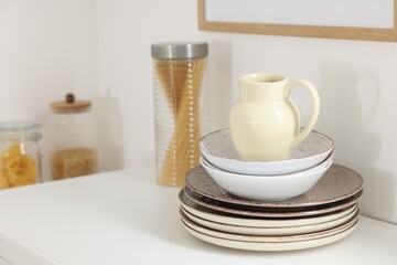 Clean ceramic jug, bowls and plates on white table in kitchen, space for text