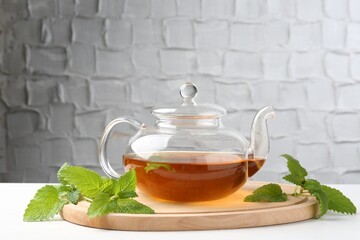 Aromatic lemon balm tea in glass teapot and fresh leaves on white table against light background