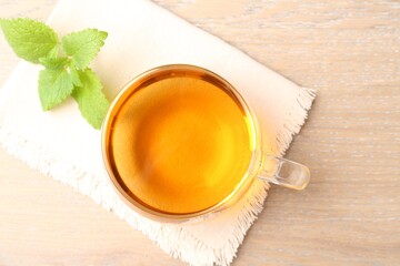 Aromatic lemon balm tea in glass cup and fresh leaves on wooden table, flat lay