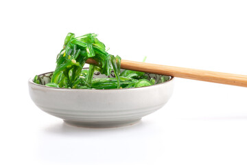 Chopsticks holding Japanese seaweed salad. Japanese cuisine - Wakame salad, Chuka seaweed salad isolated on a white background.
