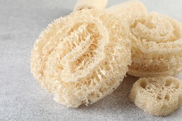 Different loofah sponges on light grey table, closeup
