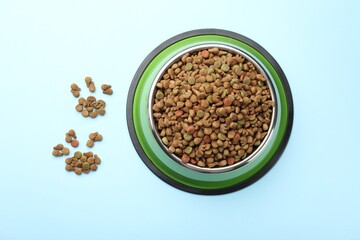 Dry pet food in feeding bowl on light blue background, top view