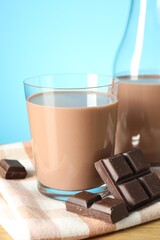 Tasty chocolate milk in glass and pieces on table against light blue background, closeup