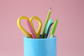 Different stationery in pen holder on pink background, closeup