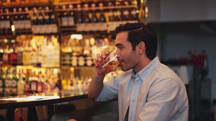 Smiling smart man drinking cocktail in Old fashioned with enjoy in cheers with friends or stranger sitting across special vibrant beverage at nightclub on Friday meeting at luxurious bar. Vinosity.