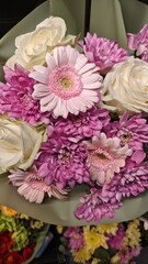 Bouquet of soft pink gerberas, purple chrysanthemums and white roses wrapped in green paper. Concept of celebration, floral gift and romantic gesture