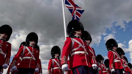 Low-angle video capturing British guards in red uniforms and bearskin hats, with a dramatic sky and Union Jack flag in the background.