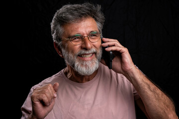 Oh, great news! Smiling young casual man talking on the phone on the dark lack background. Isolated. Chiaroscuro