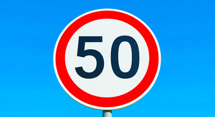 A close up of a speed limit sign with a blue sky in the background showing the speed limit of fifty
