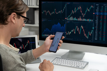 Smart stock investors pointing on screen with smartphone for market stock exchange along with laptop screen in highest dynamic investment rate, focusing data planning at modern workplace. Pecuniary.