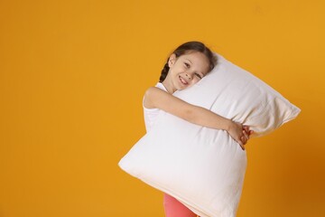 Cute girl with pillow on orange background. Space for text