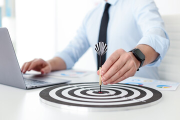 Man with dart aiming at dartboard while working indoors, closeup
