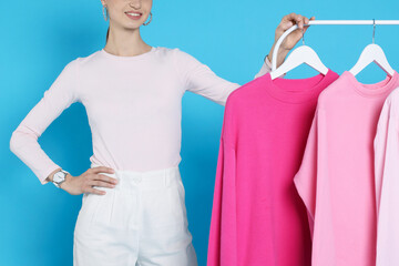 Smiling fashion stylist and rack with clothes on light blue background, closeup