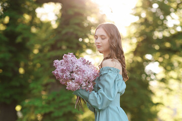Fototapeta premium Beautiful woman with bouquet of lilac flowers outdoors in morning