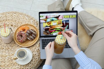 Blogger holding juice near laptop with food blog web site on floor indoors, above view