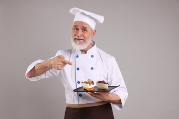 Professional pastry chef with pieces of delicious cake on grey background