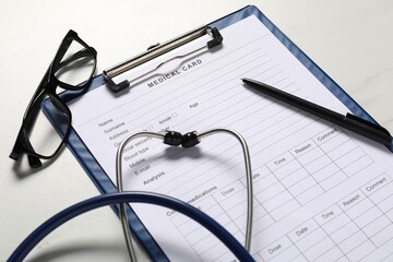 Medical card form, pen, glasses and stethoscope on white table, closeup