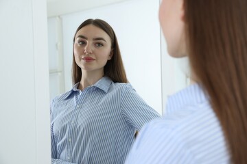 Beautiful woman looking at herself in mirror indoors