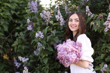 Smiling woman among lilac flowers and leaves outdoors