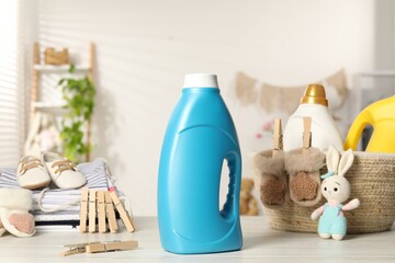 Bottles with fabric softeners, baby clothes, clothespins and toy on light wooden table indoors