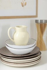 Clean ceramic jug, bowls and plates on white table in kitchen