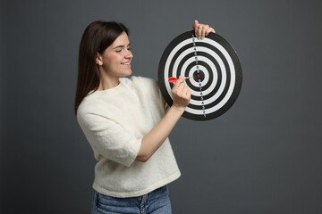 Targeting. Smiling woman with dart board and arrow on grey background