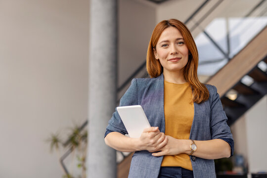 Portrait of professional businesswoman with tablet standing at enterprise with tablet in hands and smiling at camera.