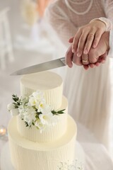 Married couple cutting delicious wedding cake with knife at table indoors, closeup