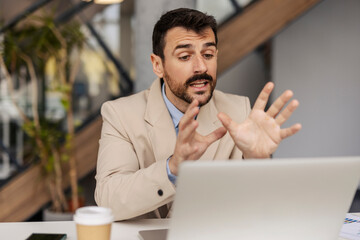 Portrait of corporate worker sitting at office and having conference call with associates on laptop.