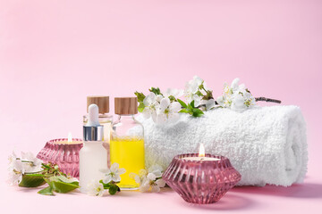 Spa composition with cosmetic products, burning candles and twigs with beautiful flowers on pink background, closeup