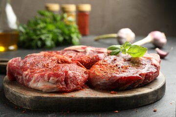 Raw steaks with spices and basil on grey table, closeup
