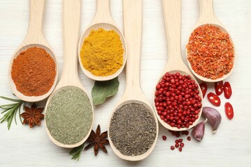Different aromatic spices in spoons on white wooden table, flat lay