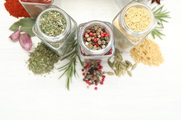 Different aromatic spices in jars on white table, flat lay