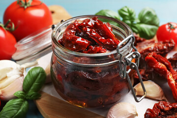 Delicious sun dried tomatoes in glass jar, fresh vegetables and spices on table, closeup